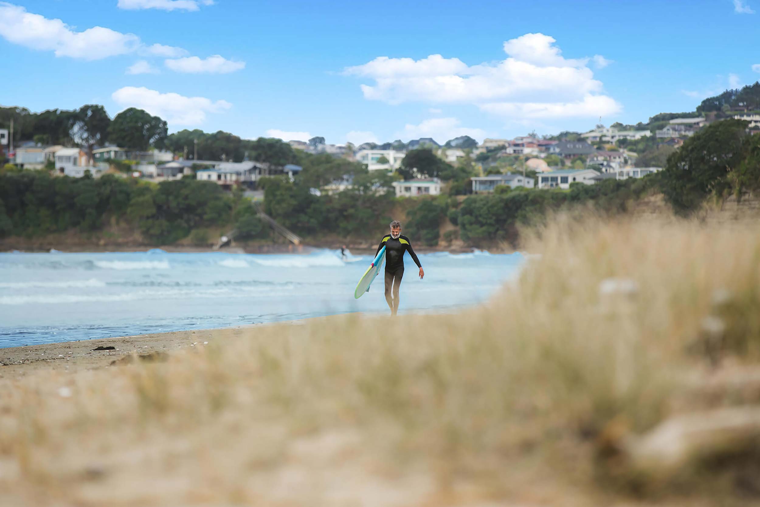 Middle-aged surfer walking on the beach carrying a surfboard