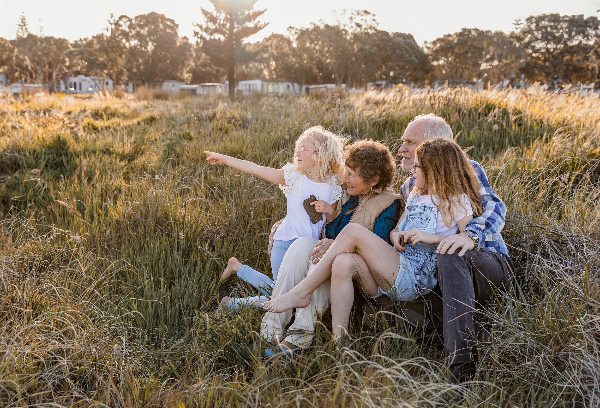 Elderly couple sitting in long grass at sunset with their grandchildren